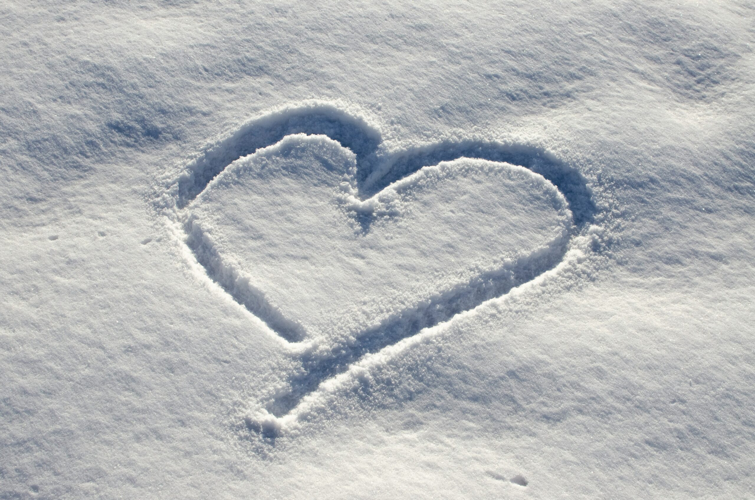 A heart shape is drawn in fresh, undisturbed snow, creating a simple and clear outline against the white, snowy surface.
